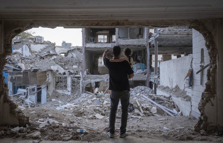 A man holds his child amid bombed-out rubble.