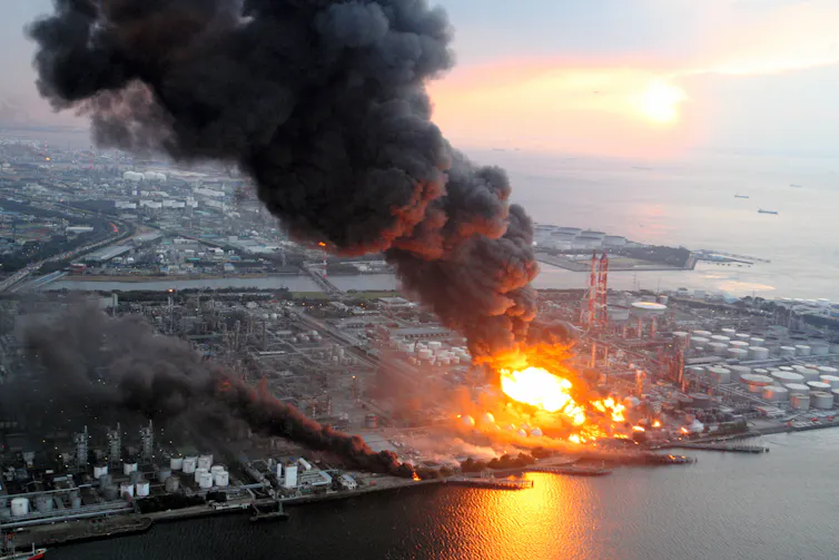 An aerial view of a burning oil refinery at the coast.