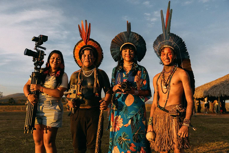 Four Indigenous storytellers in traditional dress with video camera standing outside