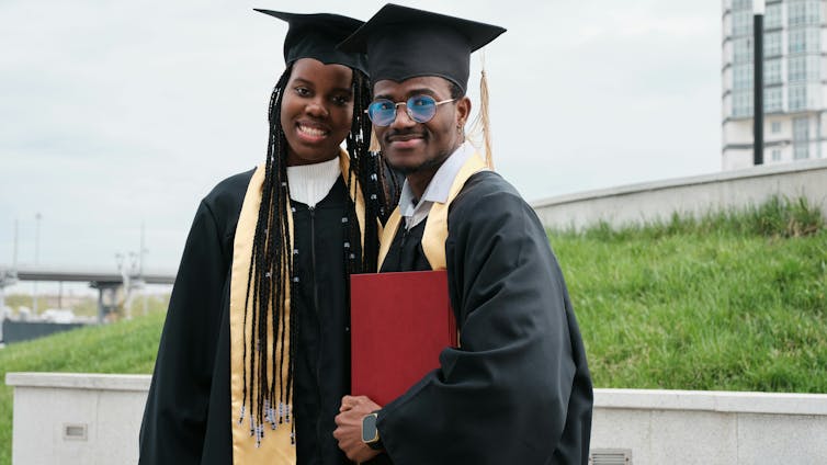 Dos graduados negros en gorras y vestidos.