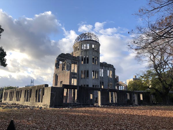 A concrete building with no windows and a metal skeleton of a dome atop a tower stand against a blue sky.