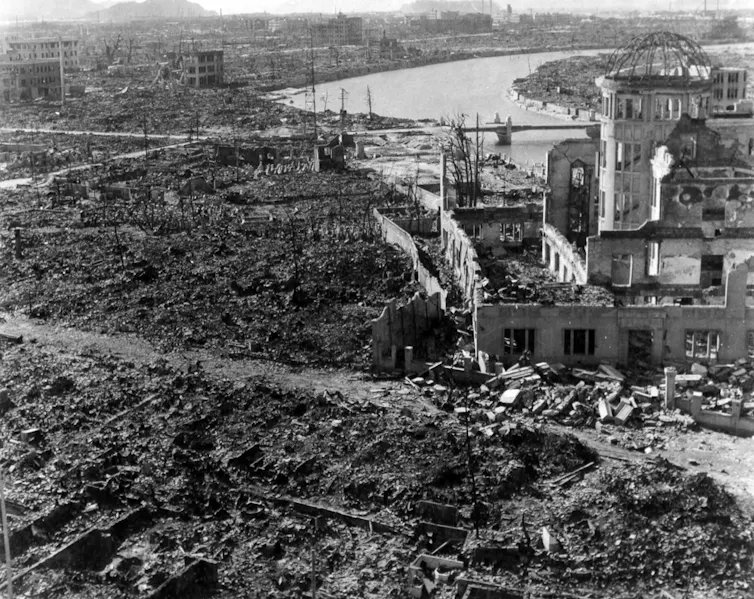Amid a landscape of rubble, a partially destroyed building stands, with the skeleton of a metal dome atop a tower.