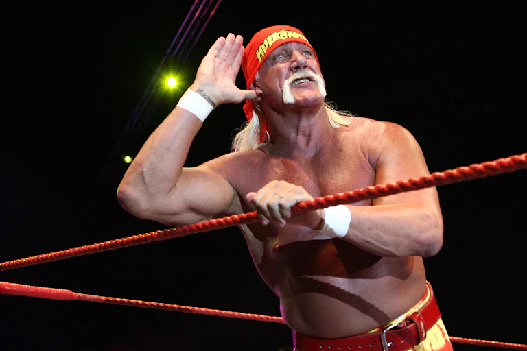 With his hand cupped to his ear, Hulk Hogan listens to the cheers of the crowd as he leans against the ropes of the wrestling ring.