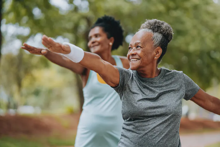 Two older women exercising together in a park.