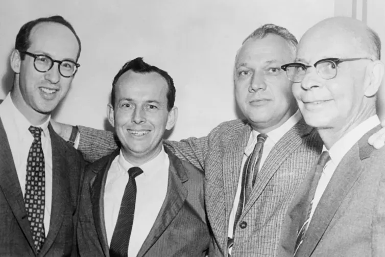Four men in suits standing together and smiling.
