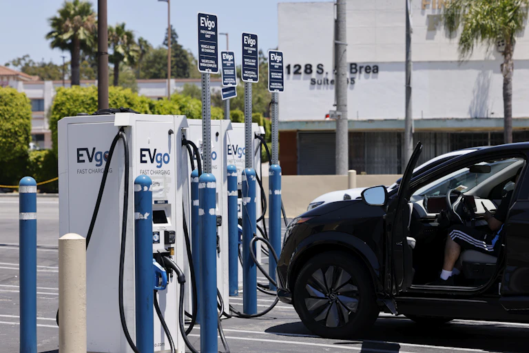 Cars are connected with cables to small towers in a parking lot.