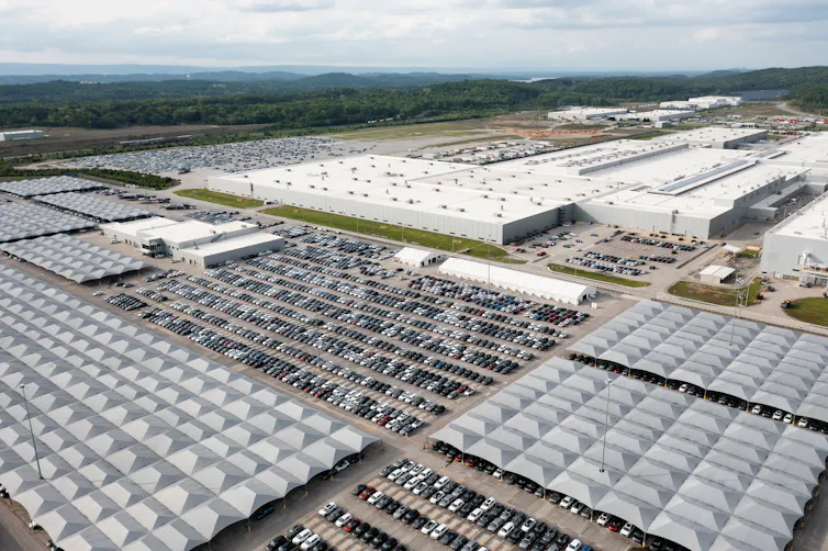 An aerial view shows a very large building with an even larger parking lot outside, filled with cars.