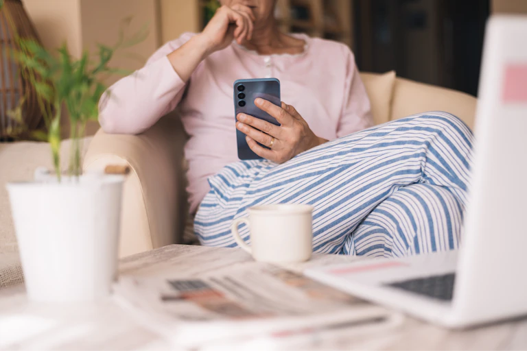 woman on a sofa wearing pyjamas and checking her phone