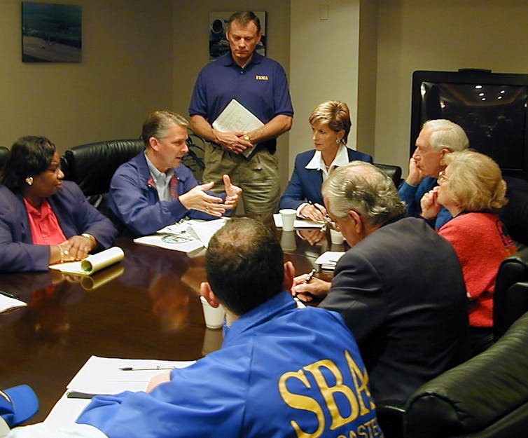 People around a table, several with government agency logos on their clothes.