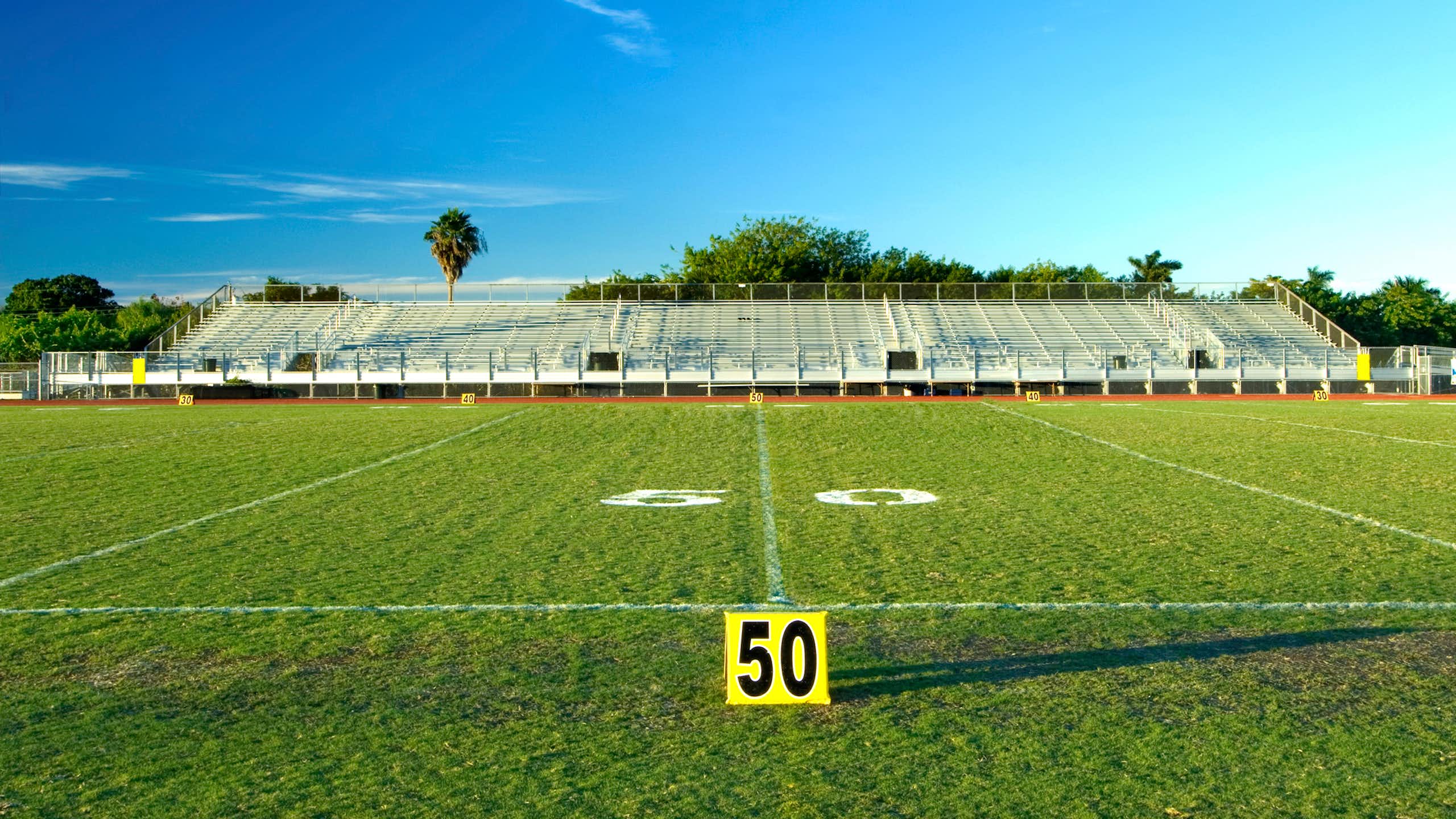An empty sports field, with bleachers in the background under a blue sky.