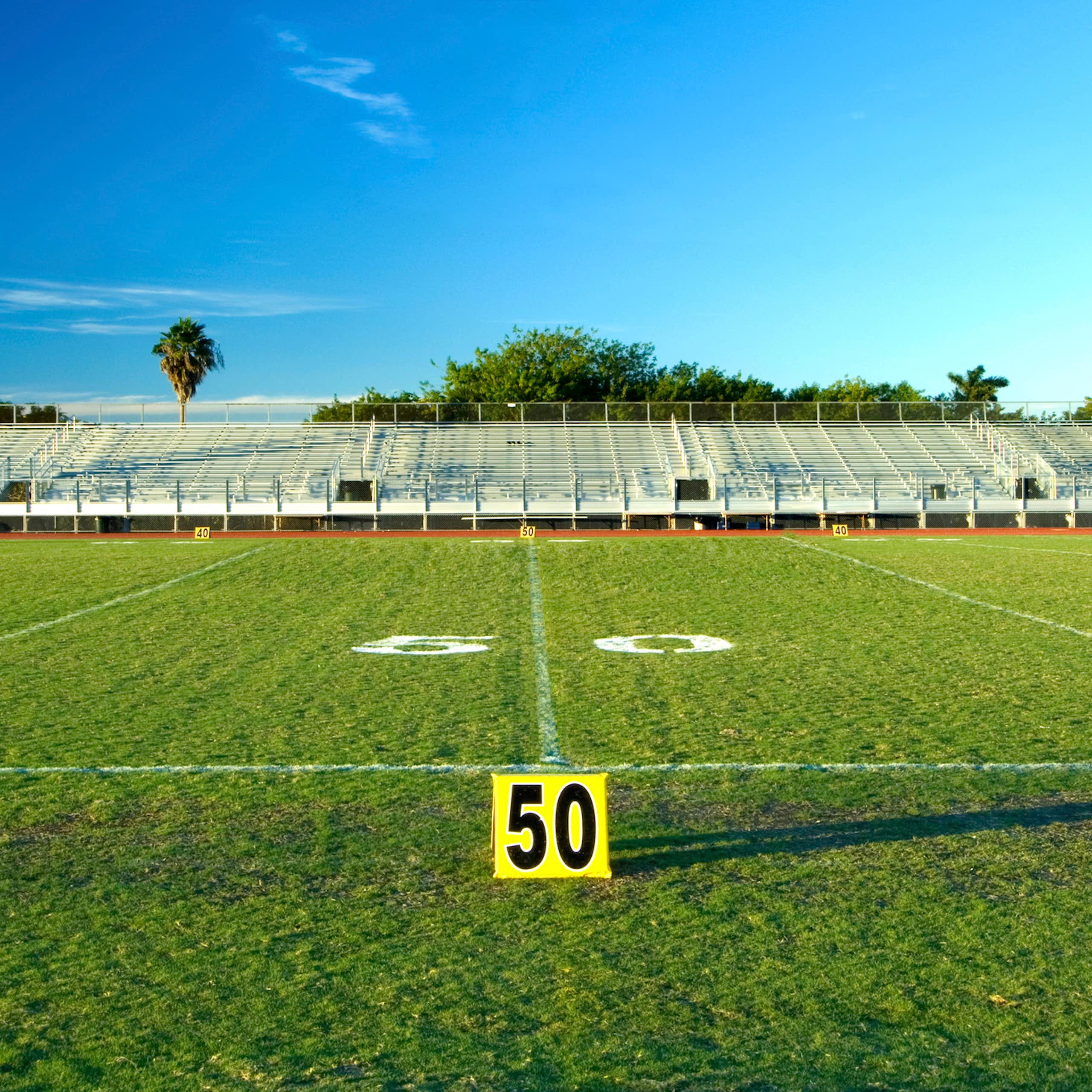 An empty sports field, with bleachers in the background under a blue sky.