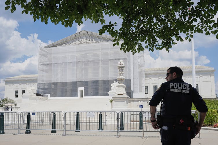 Një oficer policie me shpinë për kamerën qëndron jashtë Gjykatës së Lartë.