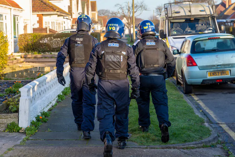 View from behind of three police officers in heavy protective gear walking down a suburban street