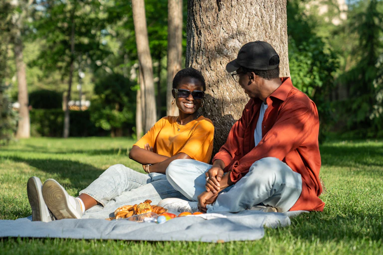 two friends chatting by tree with picnic in park