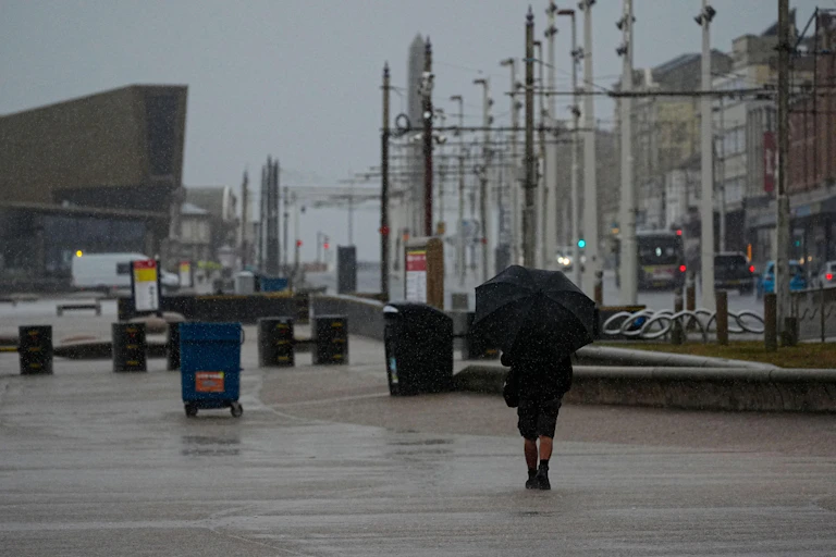 A man walks down a coastal street with an umbrella under a dark sky.