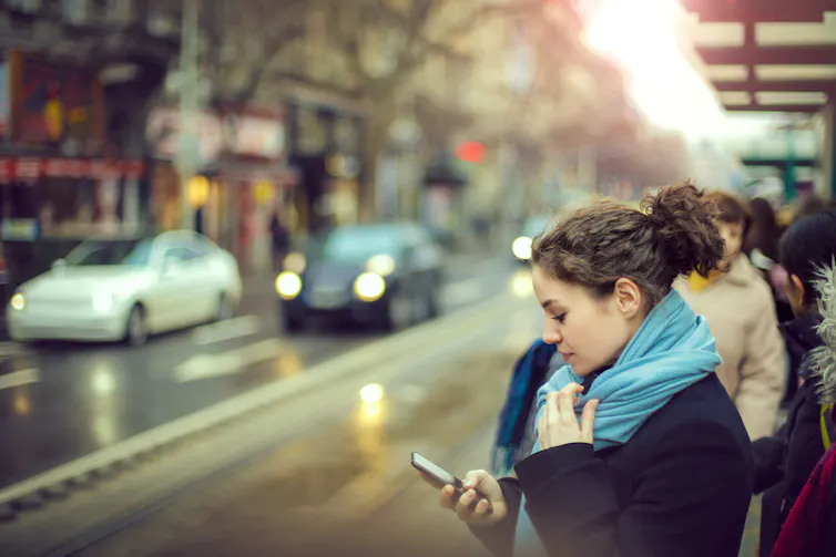 A young woman looks at her phone while waiting for the bus.