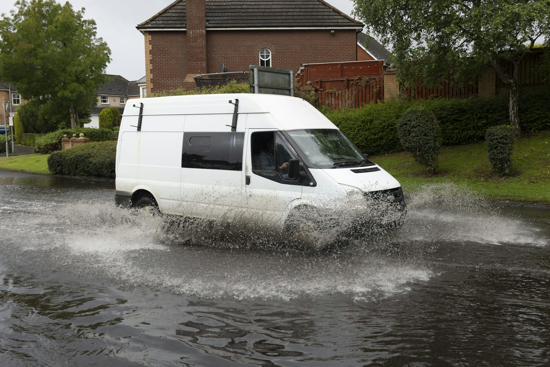 A white van driving through a flooded road.
