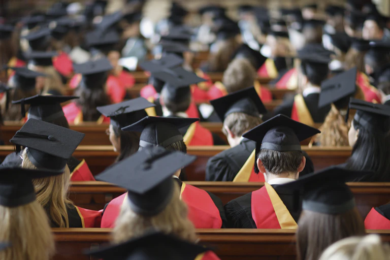 Vue de dos d'étudiants lors de la cérémonie de remise des diplômes, portant le traditionnel chapeau rectangulaire que l’on a l’habitude de voir dans les films américains.