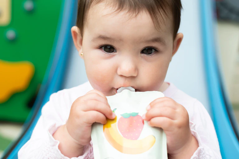 Baby eating fruit puree from food pouch outdoors
