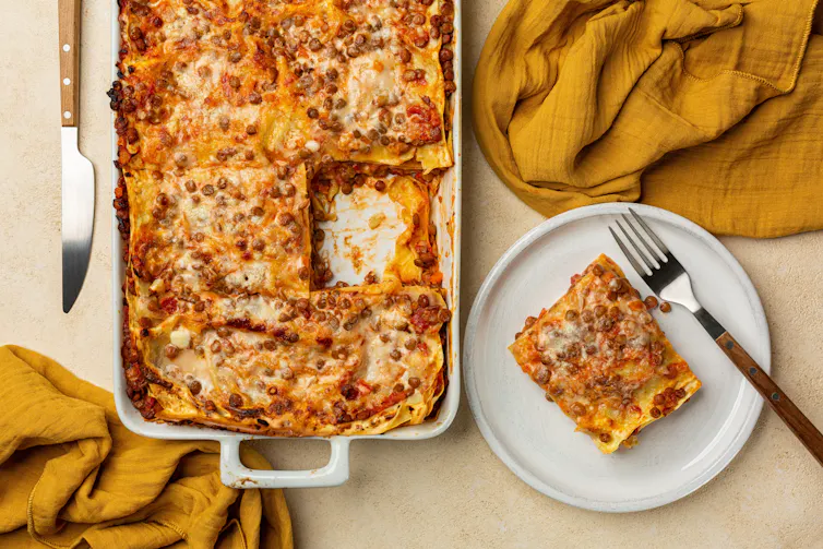 flat lay shot of lentil lasagne, portion on plate, yellow cloth on table