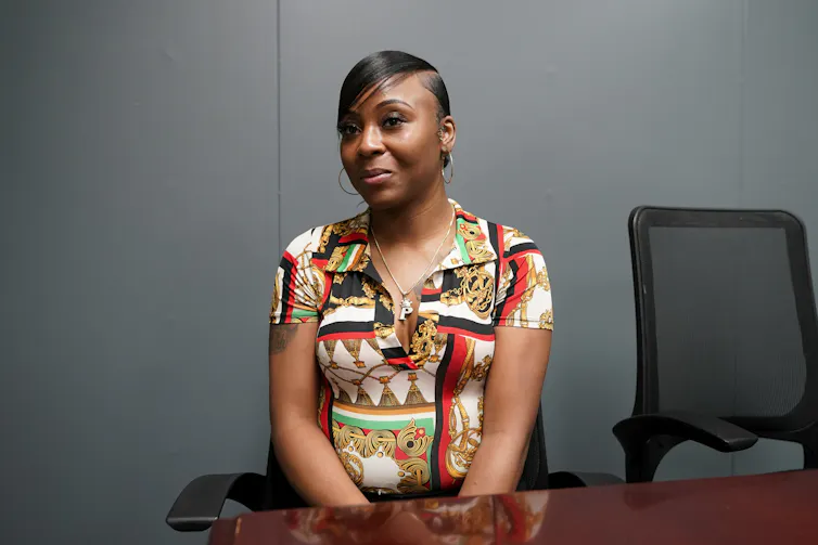 a Black woman with short hair and hoop earrings sits at a conference table