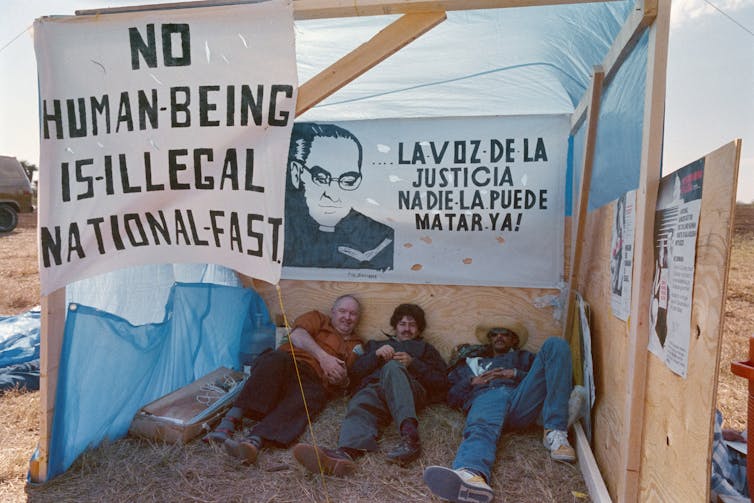 Three men lay down inside a makeshift shelter.