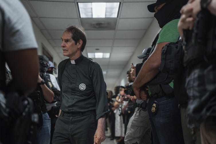 A priest walks inside a crowded hallway.
