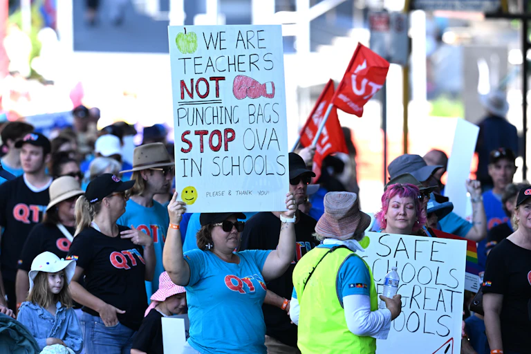 People at a rally. A woman holds a sign 'we are teachers not punching bags'