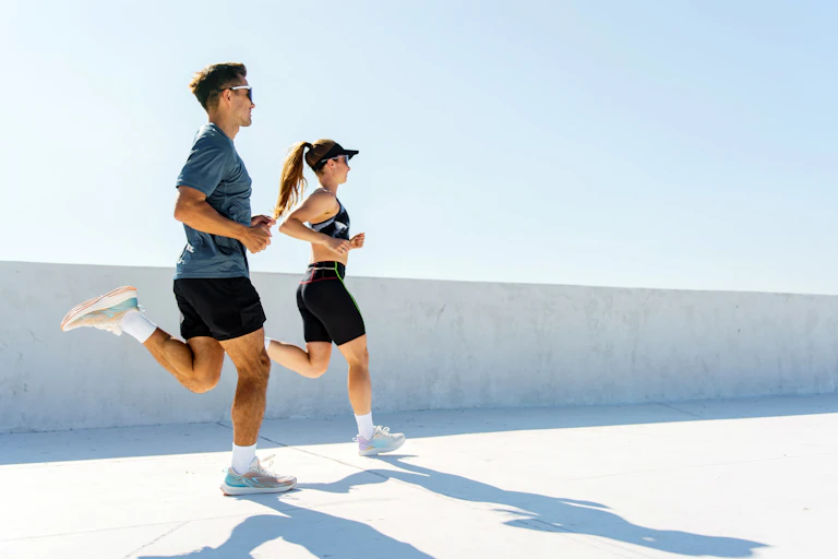 Man and woman run on a white esplanade.