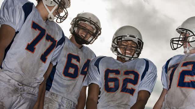 A group of high school age football players in white sports uniform and protective helmets