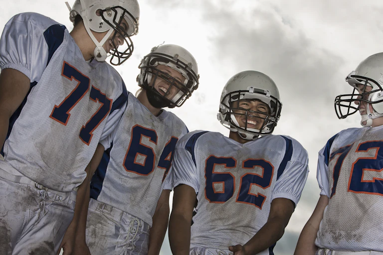 A group of high school age football players in white sports uniform and protective helmets