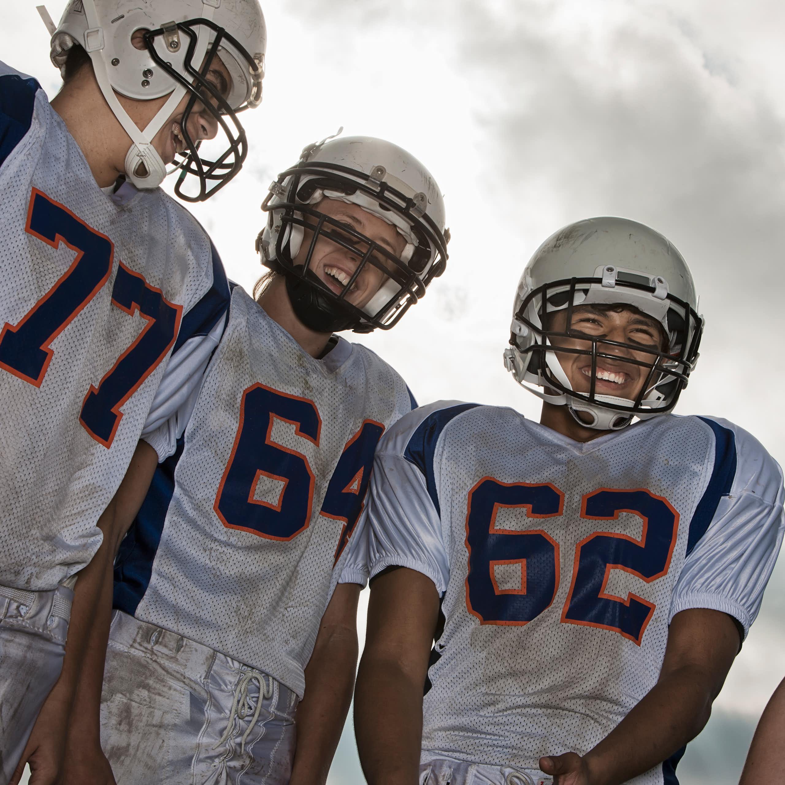 A group of high school age football players in white sports uniform and protective helmets