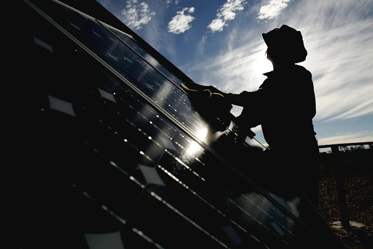 A person in silhouette wipes down solar panels