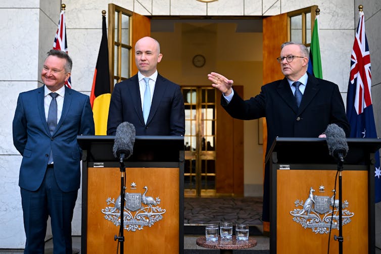 Three men in suits stand at lecterns