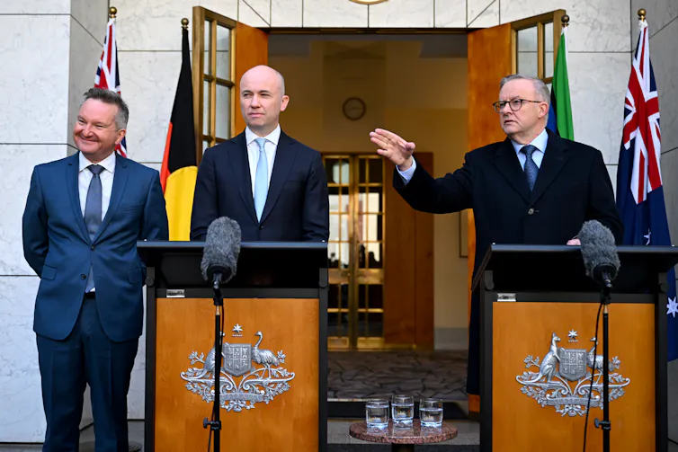 Three men in suits stand at lecterns
