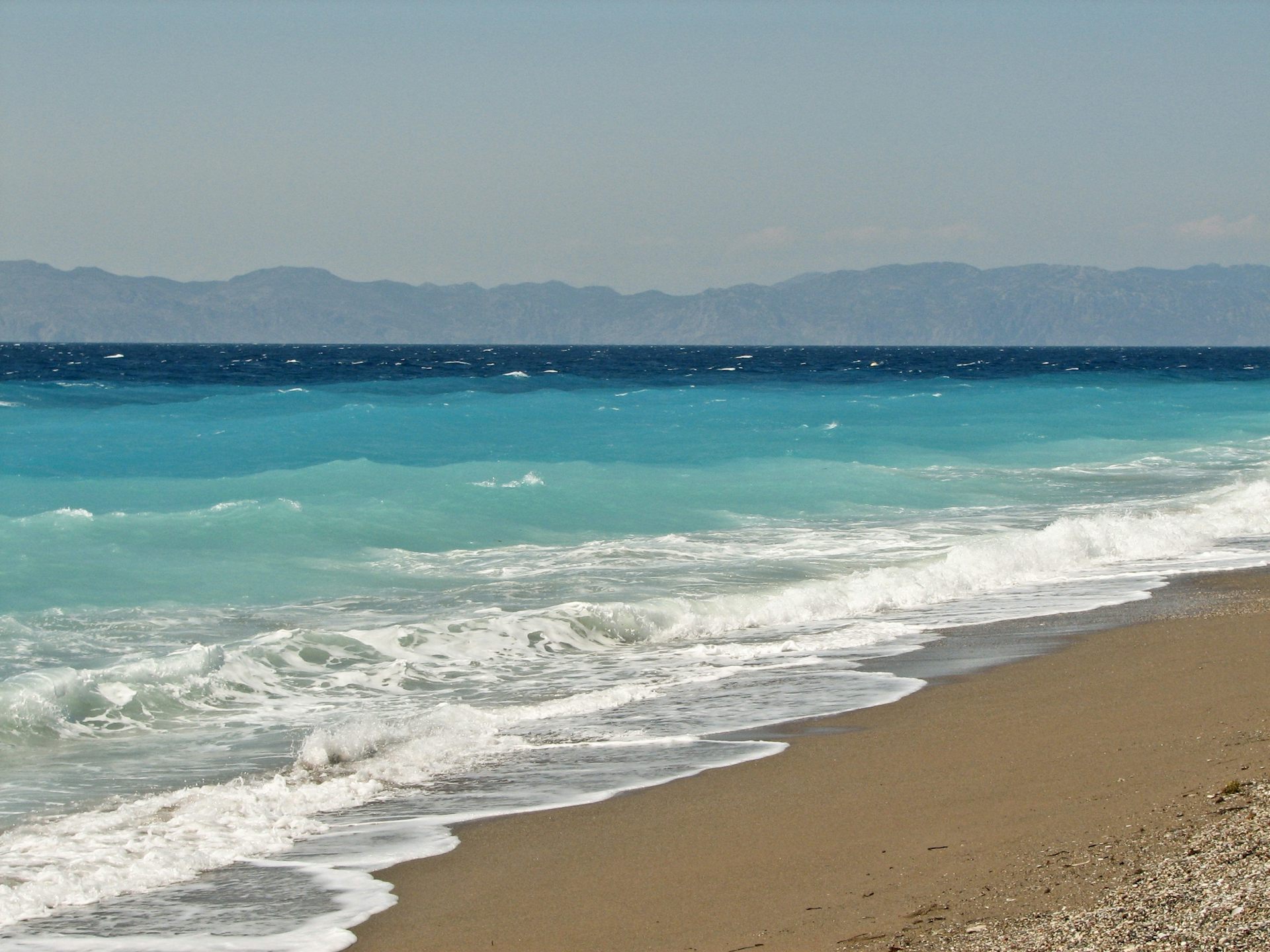 Beach with surf breaking, waves and a distant coast on the horizon