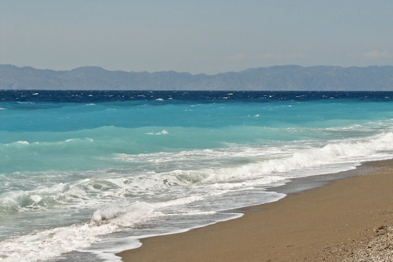 Beach with surf breaking, waves and a distant coast on the horizon