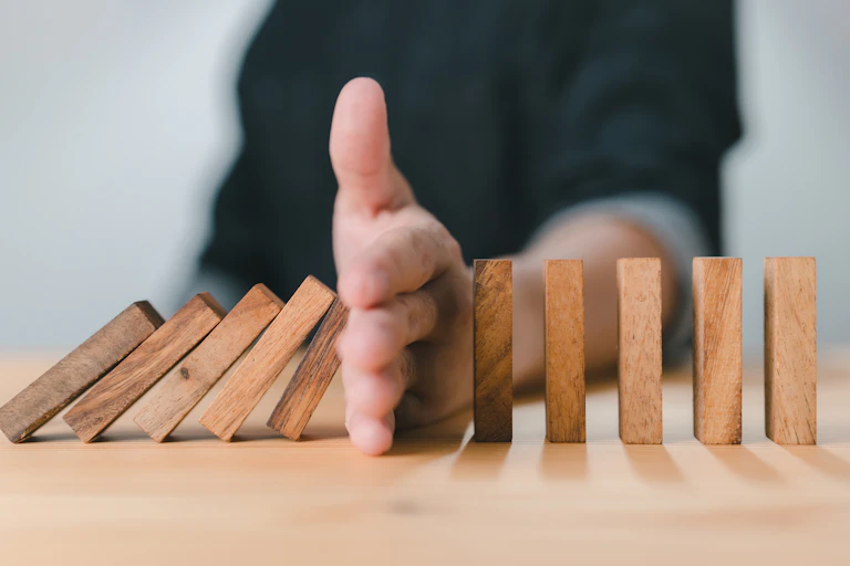 A hand stops the domino effect as a series of wooden blocks fall.