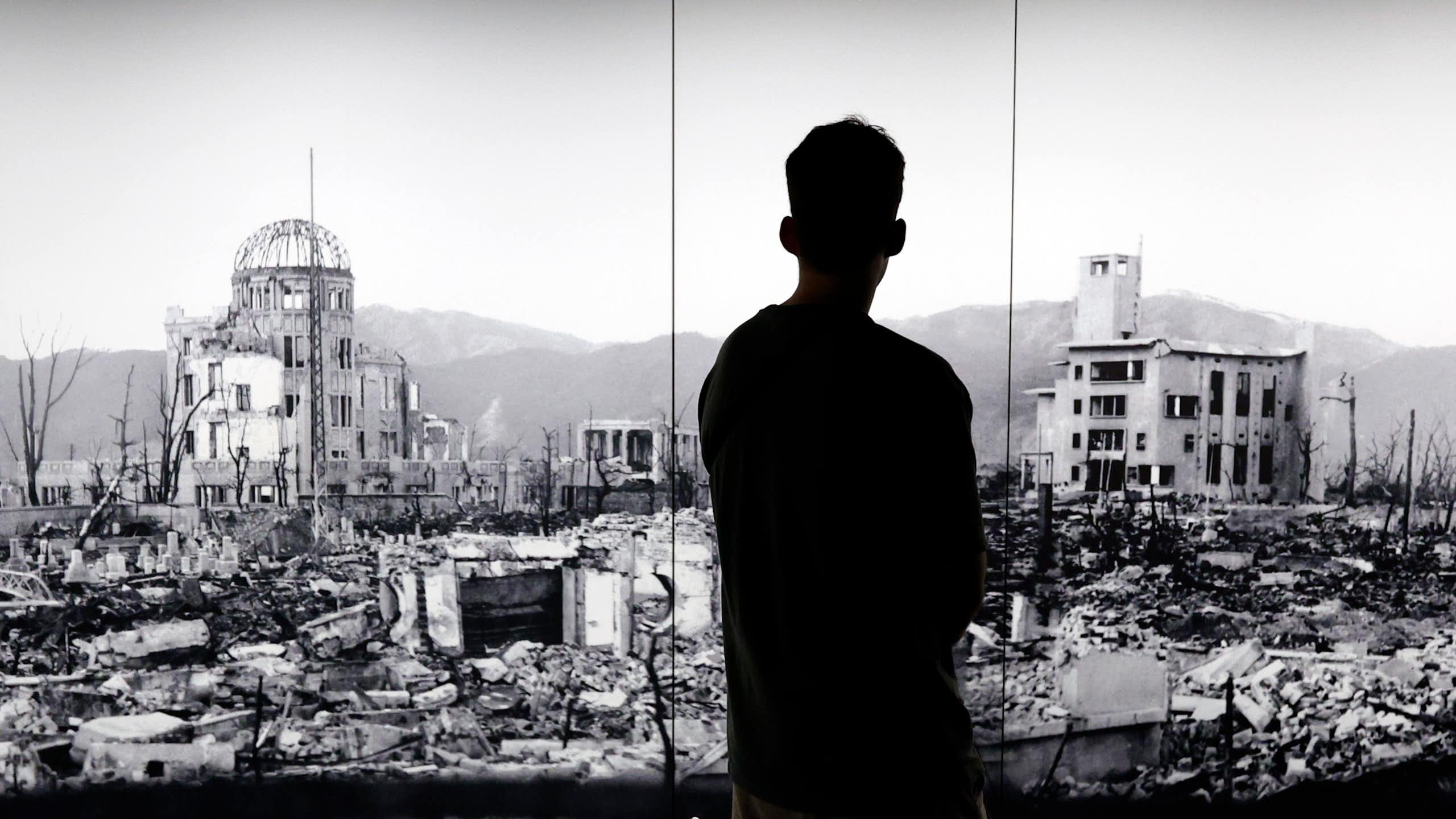 The silhouette of a man looking at a picture of Hiroshima devastated by the world's first atomic bombing.