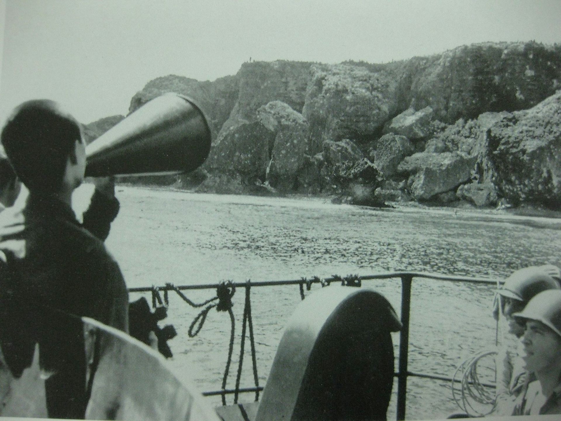 Archival photograph of a Japanese POW shouting through a loudhailer from a ship to an island.