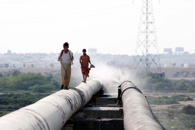 Two children walking along a burst water pipeline in Karachi.