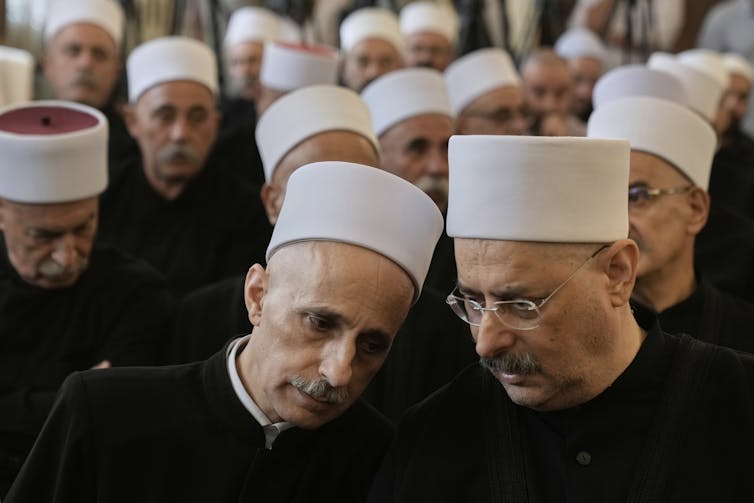 Several men, who are wearing white round hats, seem to be in deep conversation with one another.
