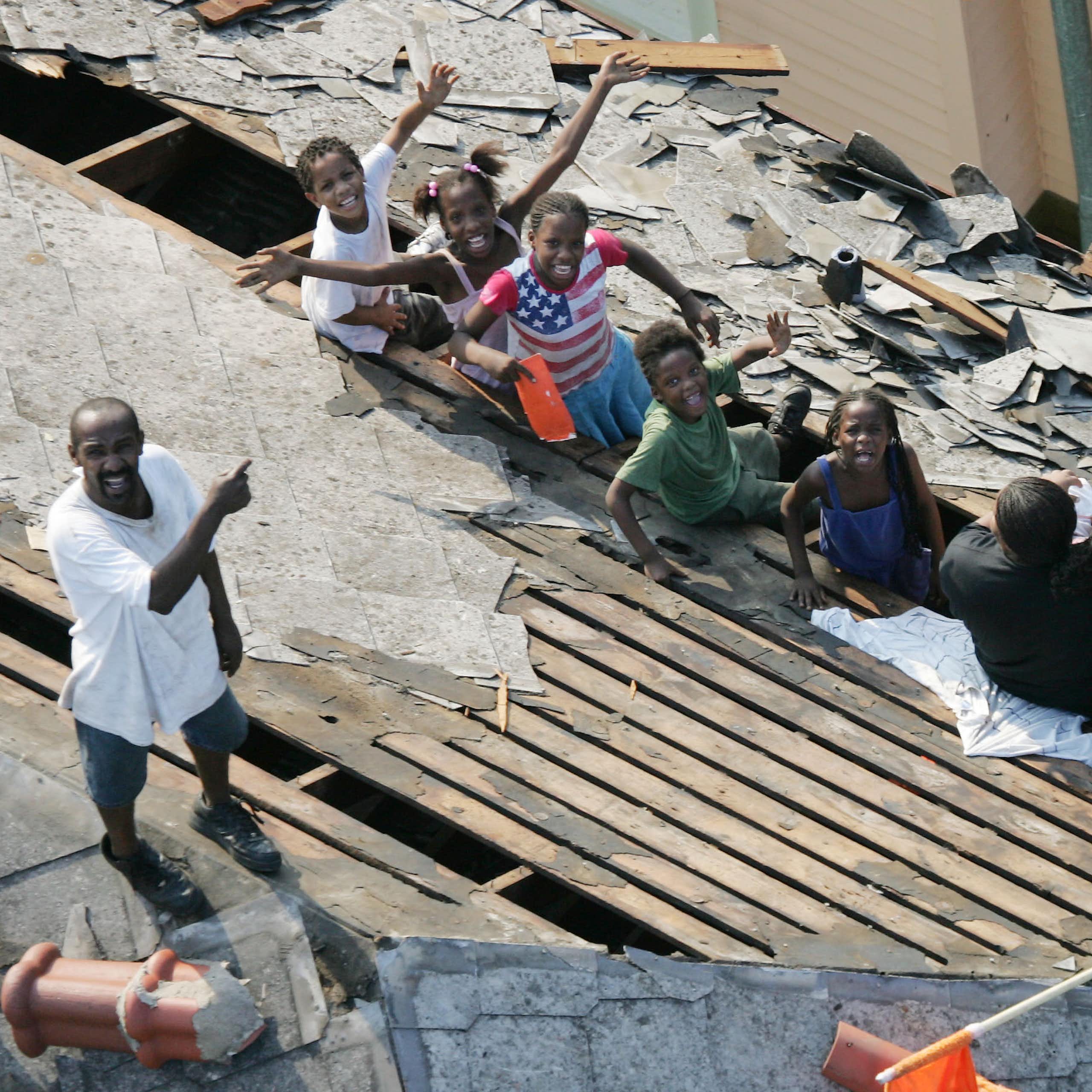 Two men, a woman and six children wait to be rescued from a rooftop. The children wave at a helicopter arriving.