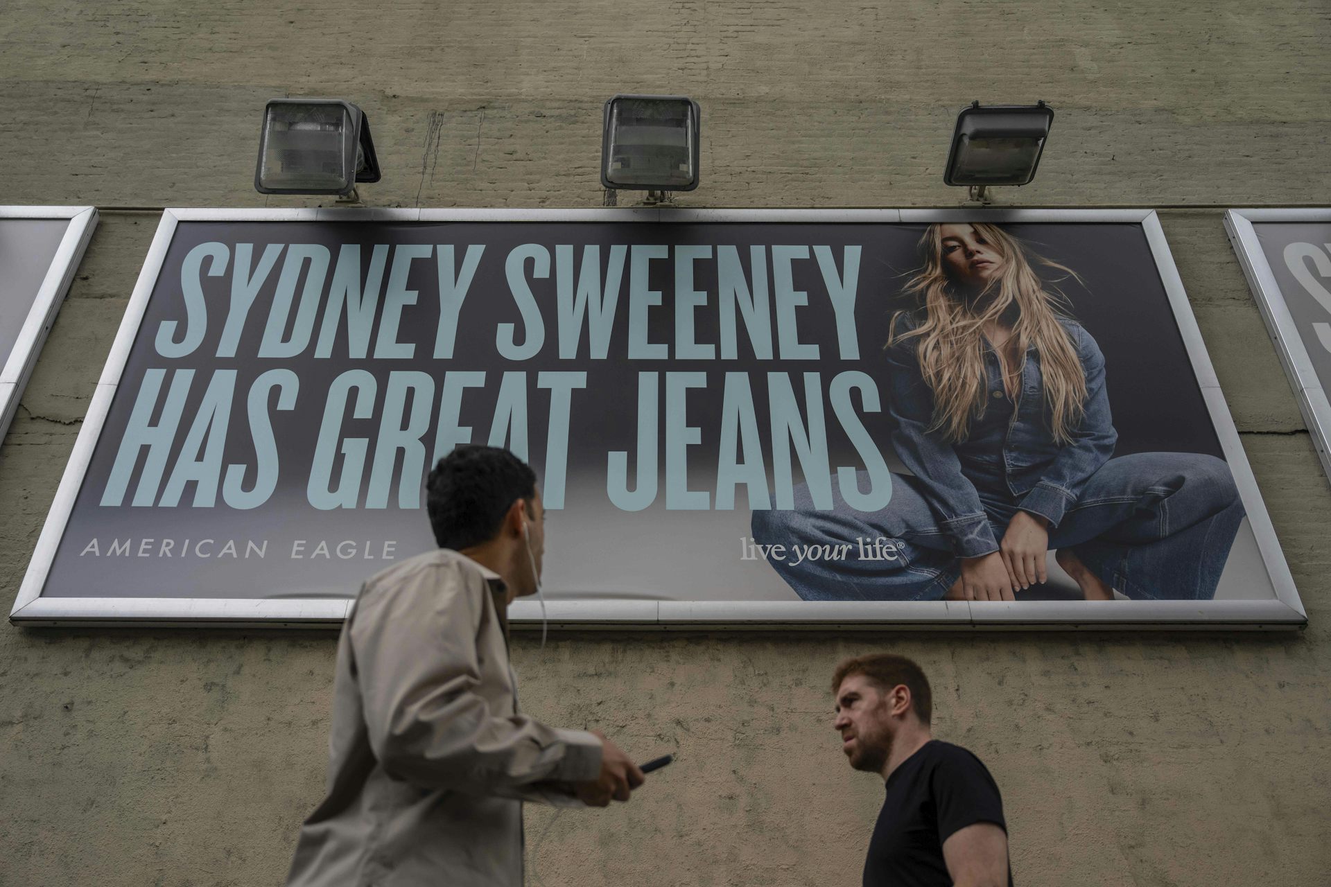 A person looks up at an advertisement that says 'Sydney Sweeney has great jeans' alongside a picture of a blonde woman in denim jeans and a jacket