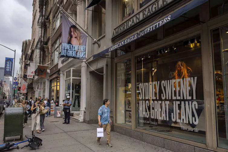 A storefront that has 'Sydney Sweeney has great jeans' printed across the front in front of an image of a blonde woman. A poster hanging outside the store says the same thing