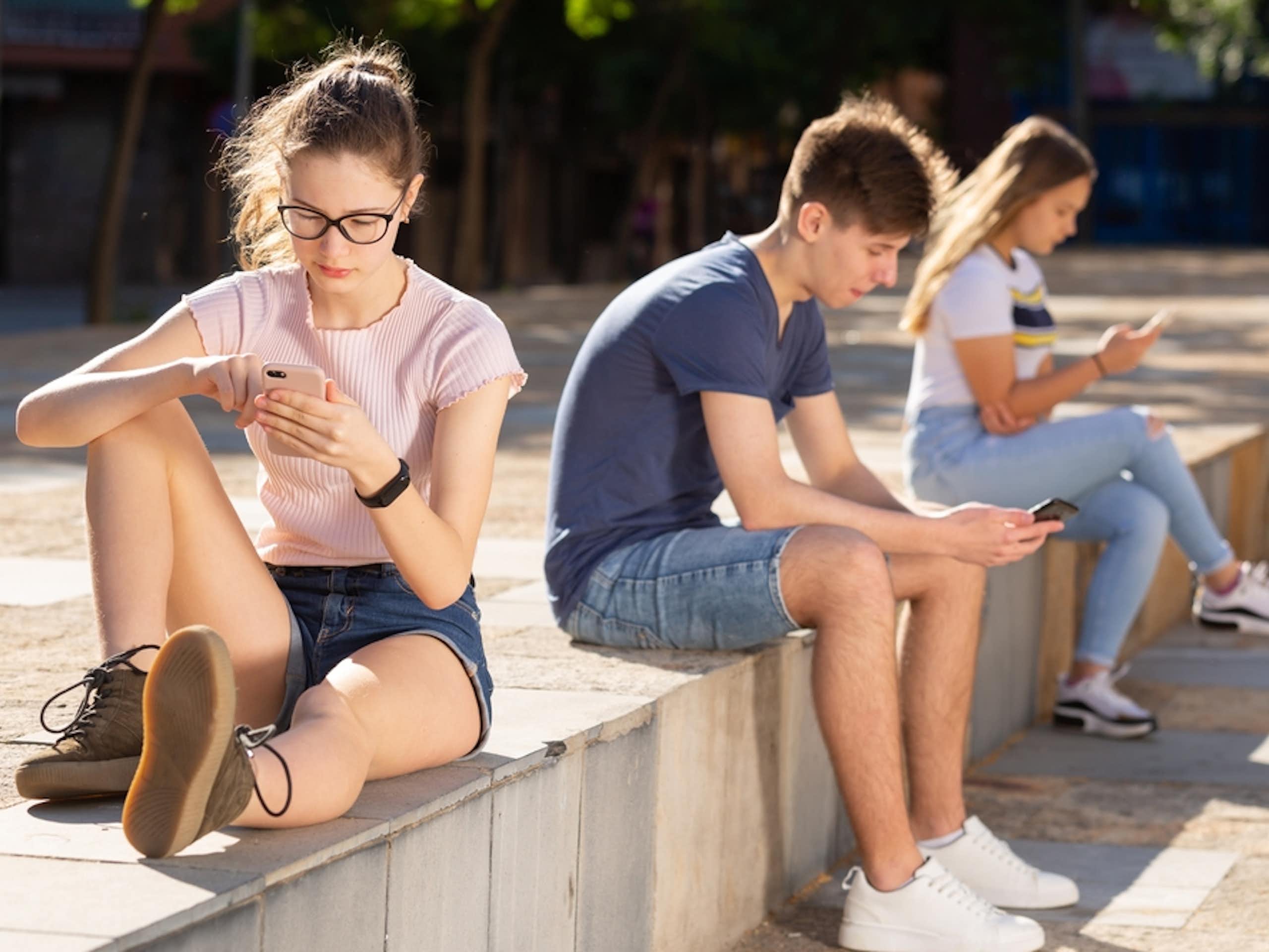 Three teens are focused on their phones.