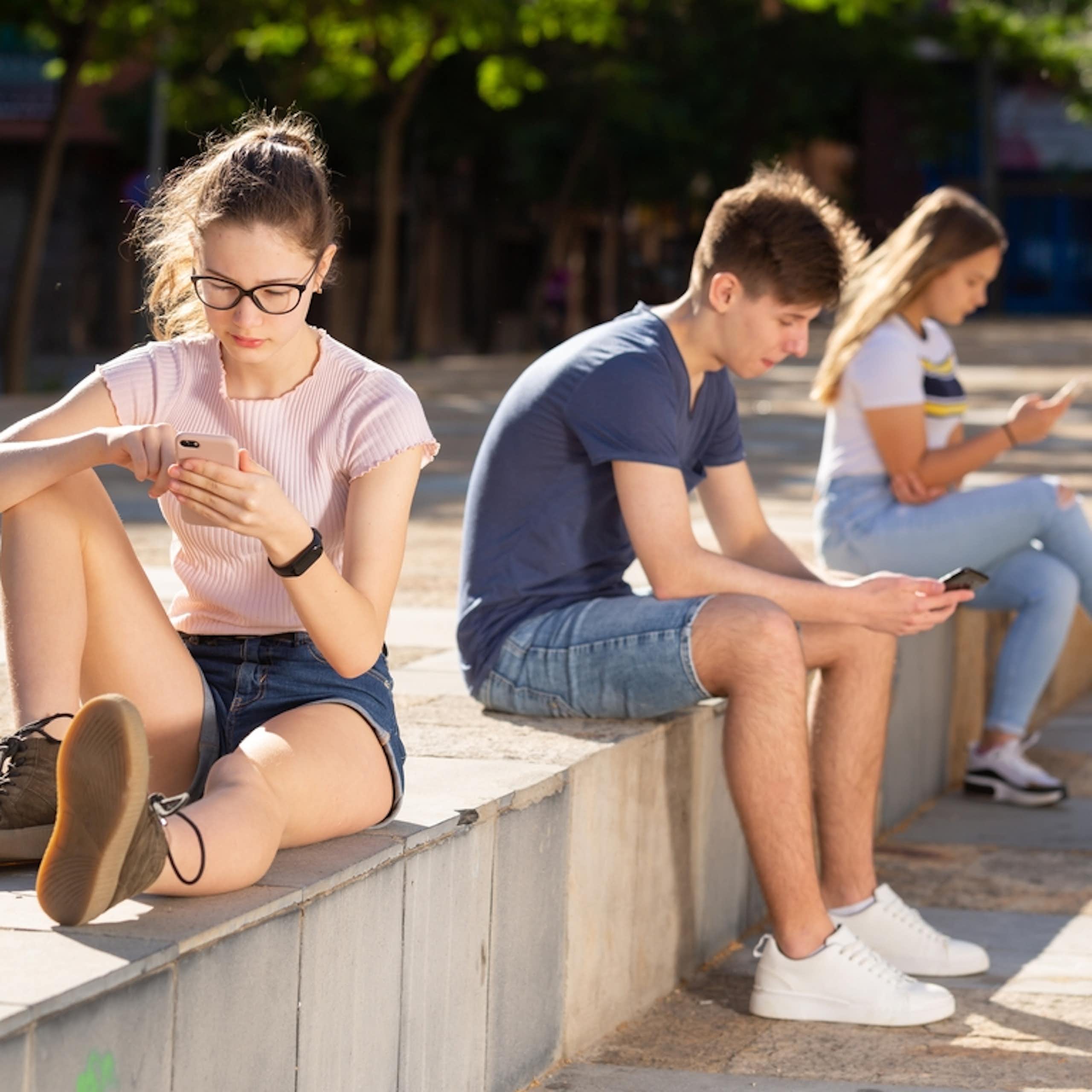 Three teens are focused on their phones.