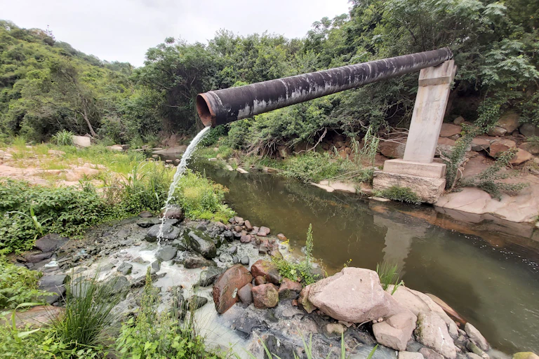 A sewage pipe juts out into the air and dirty wastewater spills from it into a stream