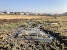A square manhole on the ground that is spewing sewage, turning the nearby land into a swampy area