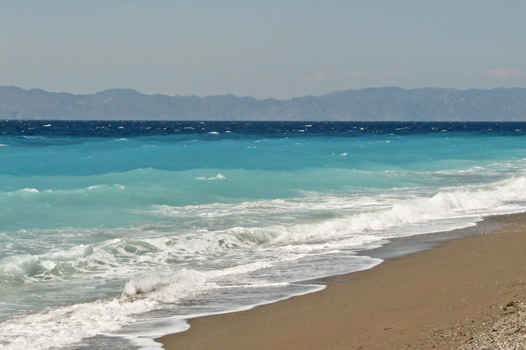 Playa con olas rompiendo, olas y una costa lejana en el horizonte.